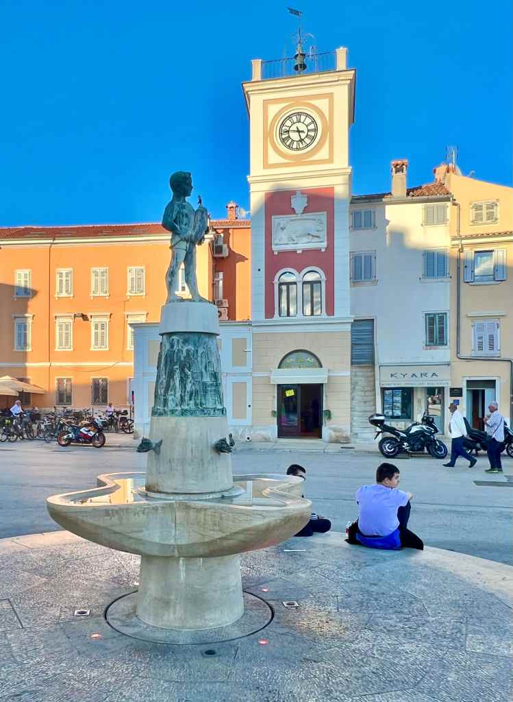 Fountain and Town Hall at Marshal Tito Square in Rovinj, Croatia. The bronze statue of a little boy holding a fish was built in 1959 to commemorate Rovonj first got running water.